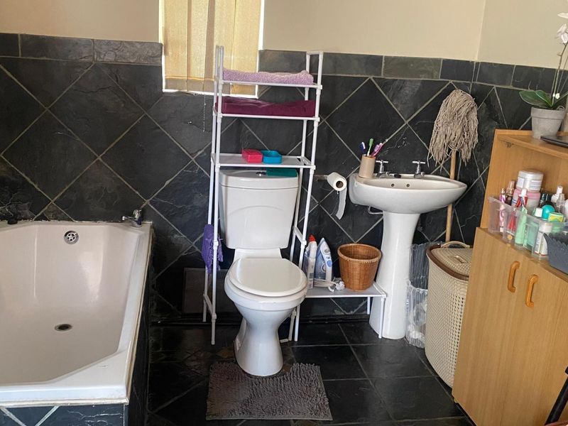A functional bathroom featuring a built-in bathtub, pedestal washbasin, and toilet, finished with dark slate wall and floor tiles.