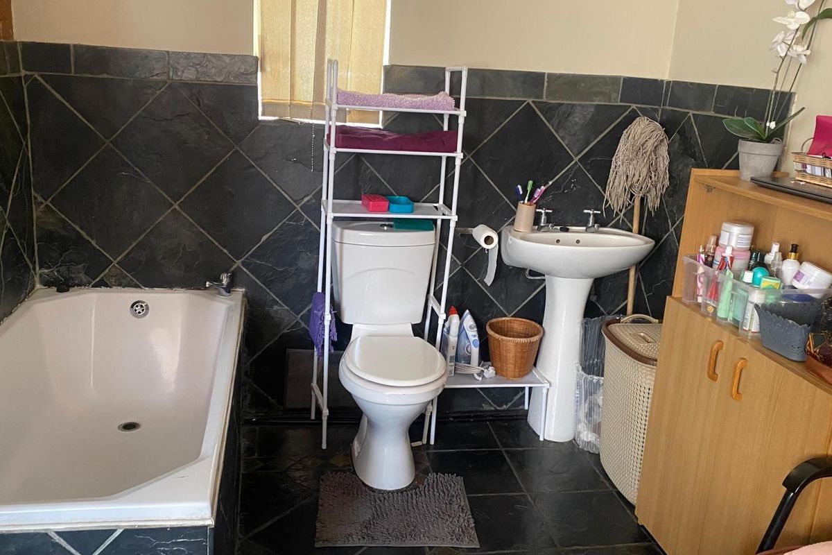 A functional bathroom featuring a built-in bathtub, pedestal washbasin, and toilet, finished with dark slate wall and floor tiles.