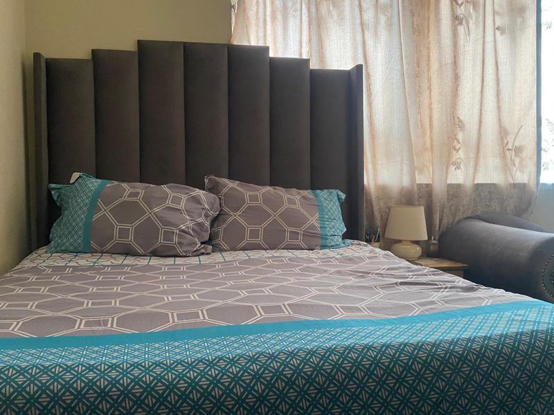 A bedroom featuring a large upholstered headboard and window with curtains.