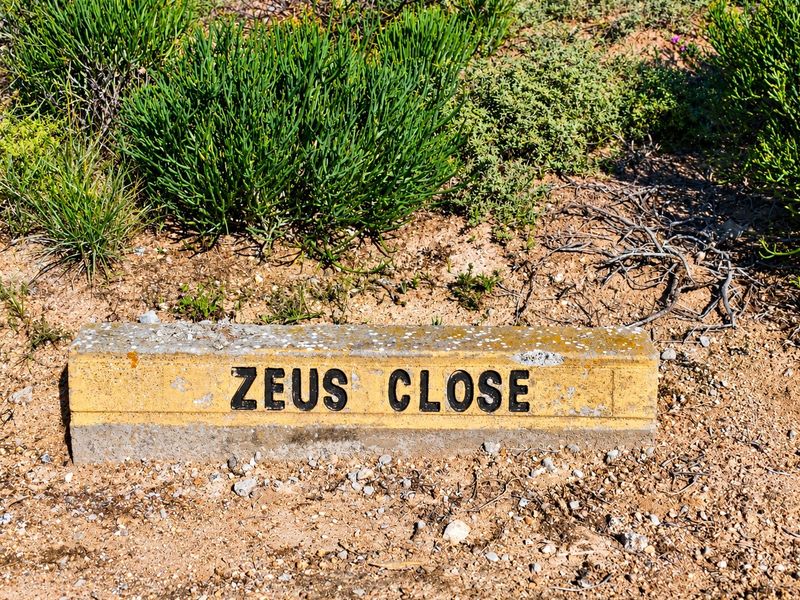 A concrete street name marker for Zeus Close situated on a vacant residential plot.