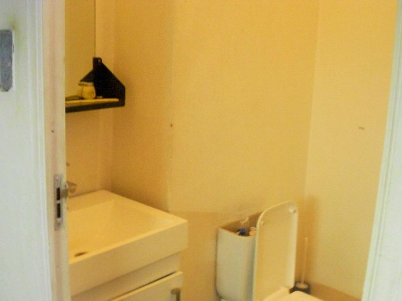 A compact bathroom featuring a wall-mounted basin with vanity storage and a standard toilet, requiring cosmetic updates to improve its overall condition.