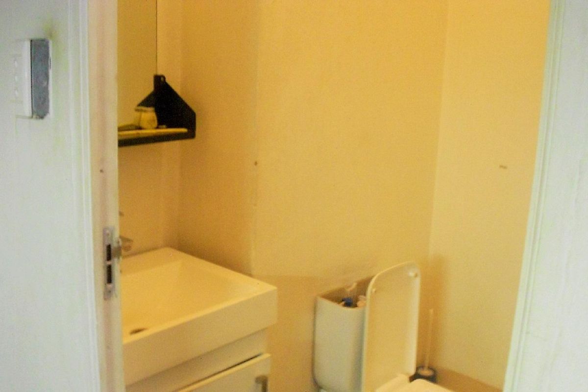 A compact bathroom featuring a wall-mounted basin with vanity storage and a standard toilet, requiring cosmetic updates to improve its overall condition.