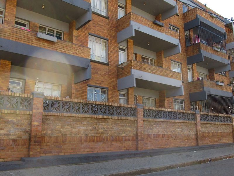 Exterior view of a multi-story brick apartment building featuring private balconies, secure perimeter walling, and street-level access.