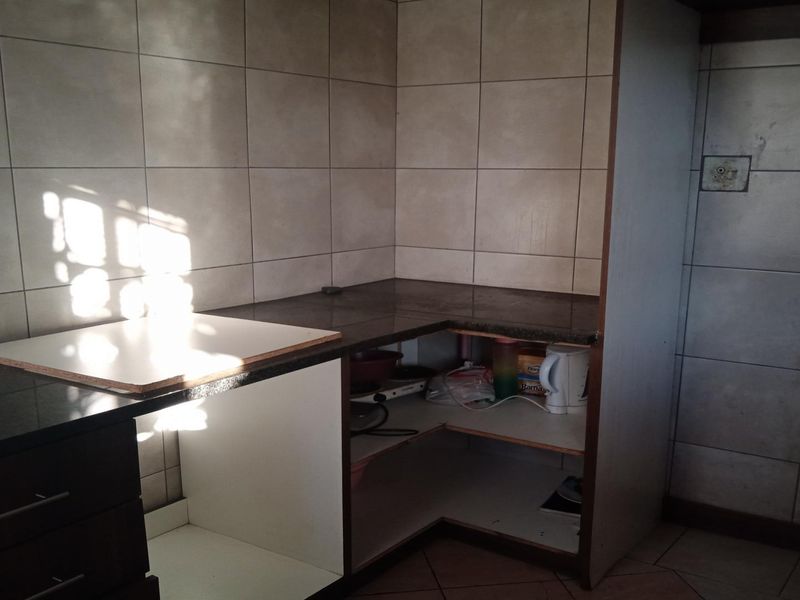 A compact kitchen area featuring tiled splashbacks, granite countertops, and built-in cabinetry, currently requiring some maintenance and cabinet door replacements.