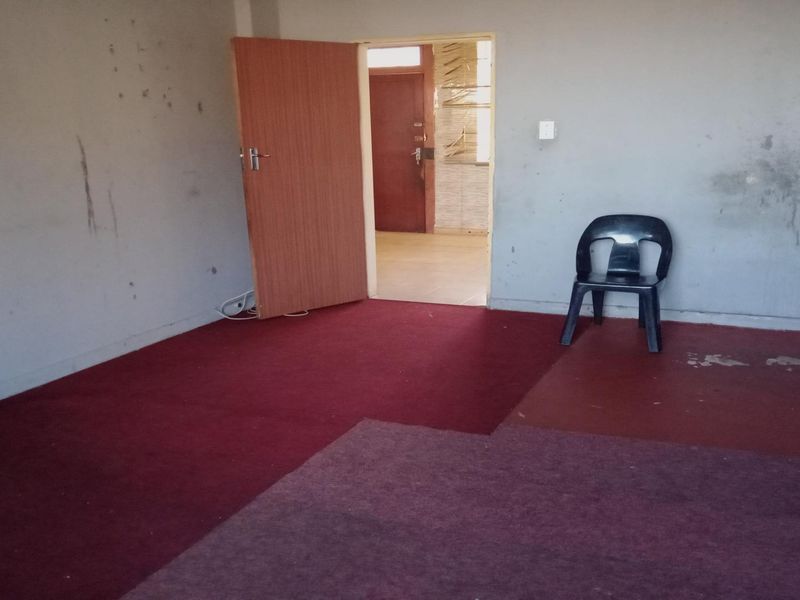 An empty living room area featuring worn carpeting and walls in need of repair, offering a blank canvas for renovation.