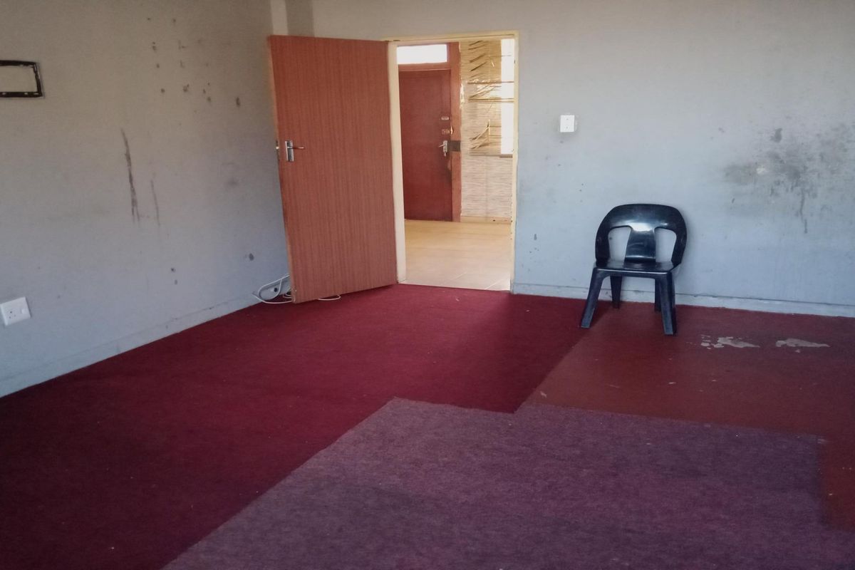 An empty living room area featuring worn carpeting and walls in need of repair, offering a blank canvas for renovation.