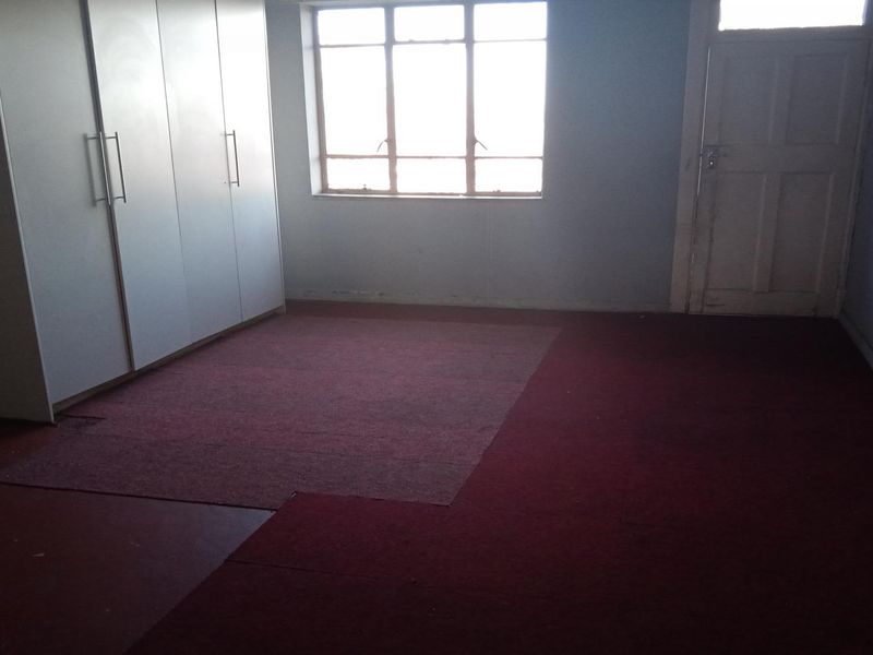 An empty bedroom featuring built-in cupboards, a multi-pane window, and worn carpet flooring in need of replacement.