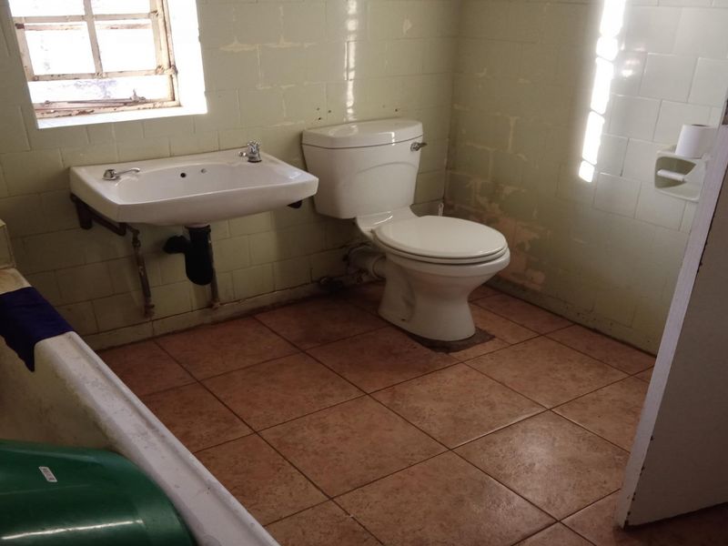 A dated bathroom featuring a wall-mounted basin, toilet, and bathtub with tiled finishes, requiring renovation to update the worn fixtures and wall surfaces.