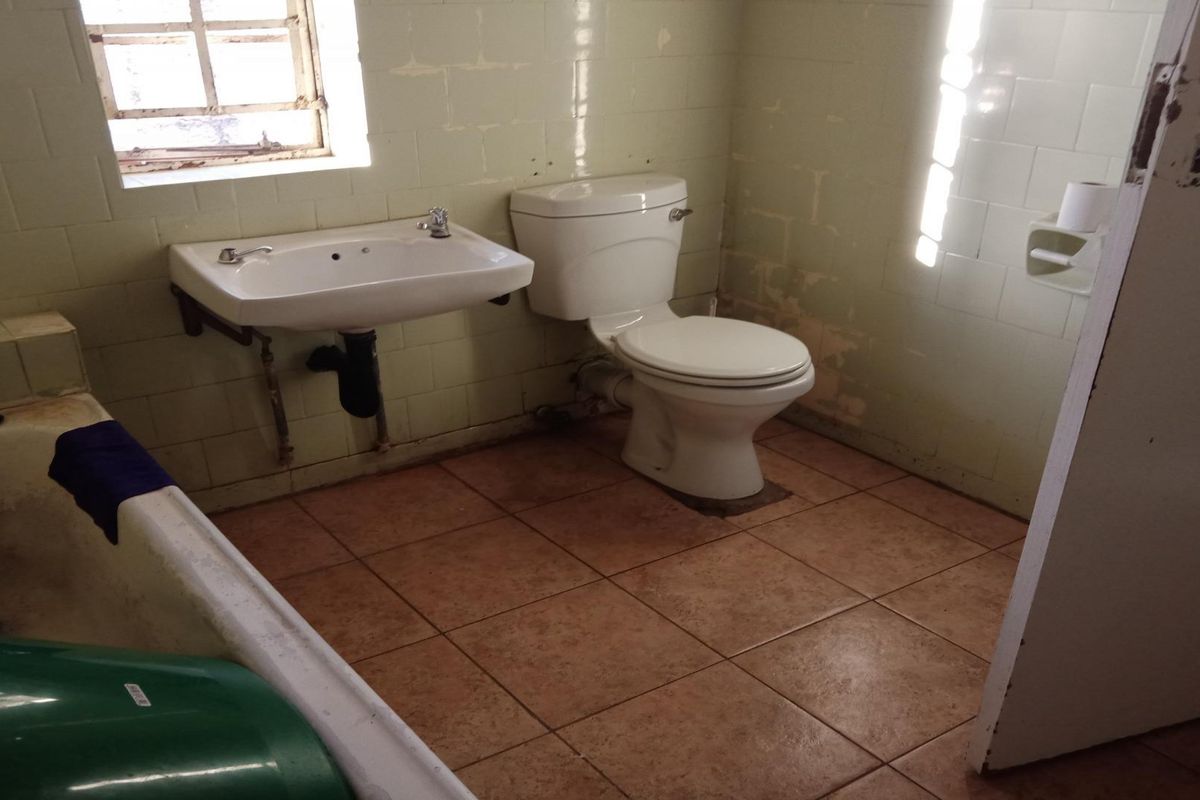 A dated bathroom featuring a wall-mounted basin, toilet, and bathtub with tiled finishes, requiring renovation to update the worn fixtures and wall surfaces.
