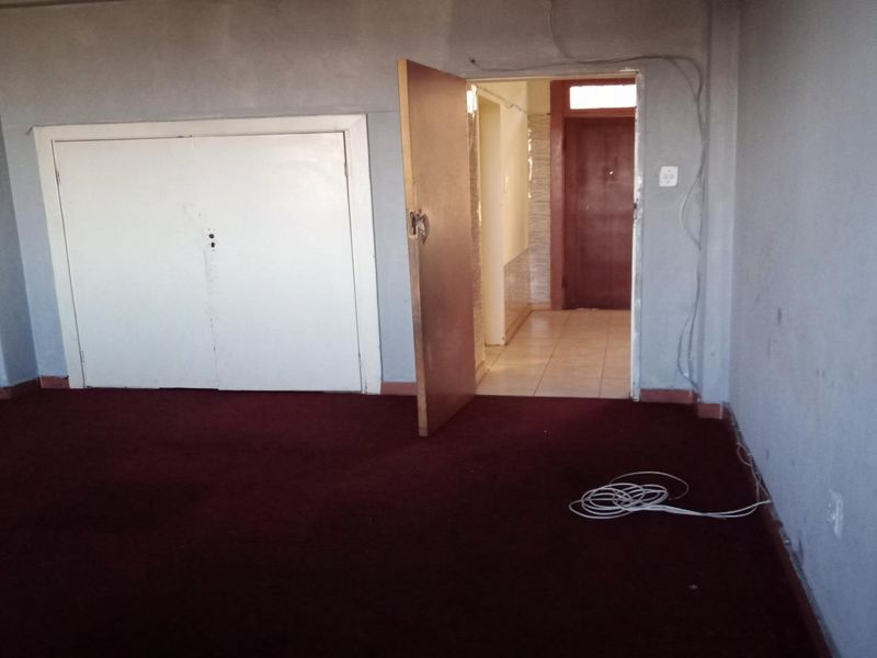 An empty bedroom featuring built-in cupboards and carpet flooring, requiring cosmetic updates and repairs to the wall finishes and electrical fixtures.