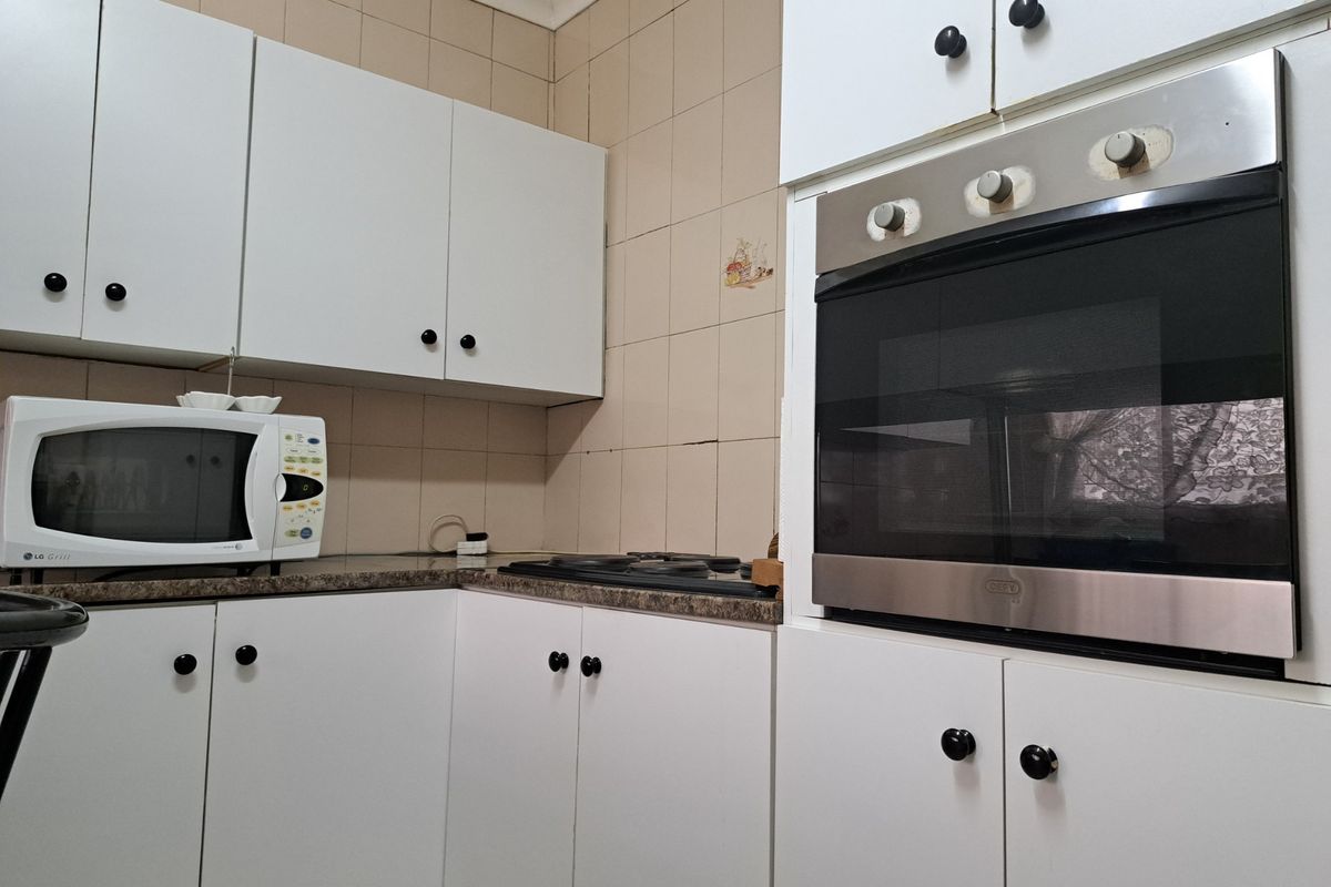 A functional kitchen featuring white built-in cabinetry, a laminate countertop, and a built-in oven with an electric hob.