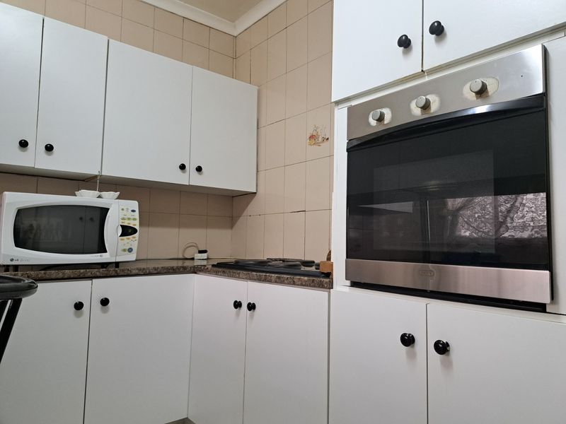 A functional kitchen featuring white built-in cabinetry, a laminate countertop, and a built-in oven with an electric hob.