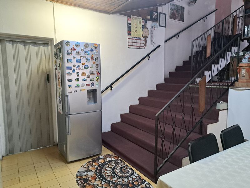 Interior hallway featuring a staircase with metal handrails, tiled flooring, and a folding door, showing signs of dated finishes and wear.