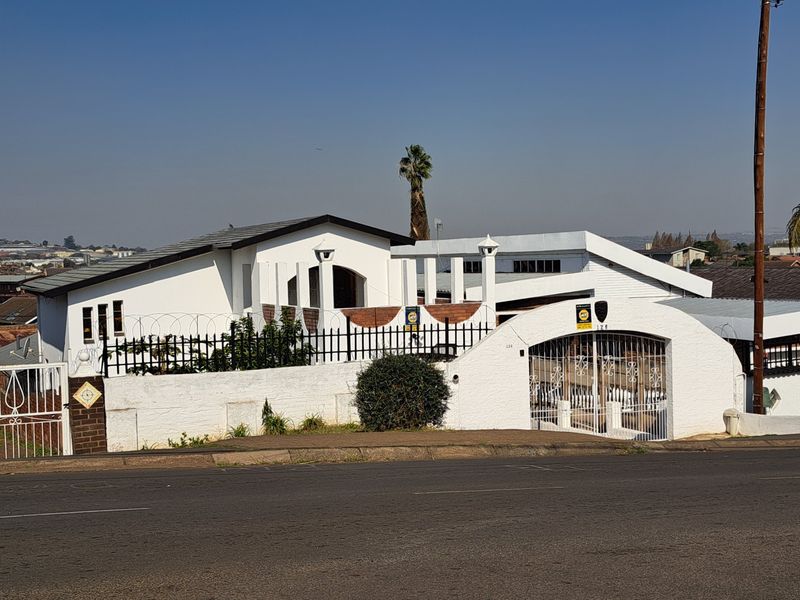 Front elevation of a residential property featuring a white rendered facade, tiled roof, secure perimeter wall with iron gates, and integrated security features.