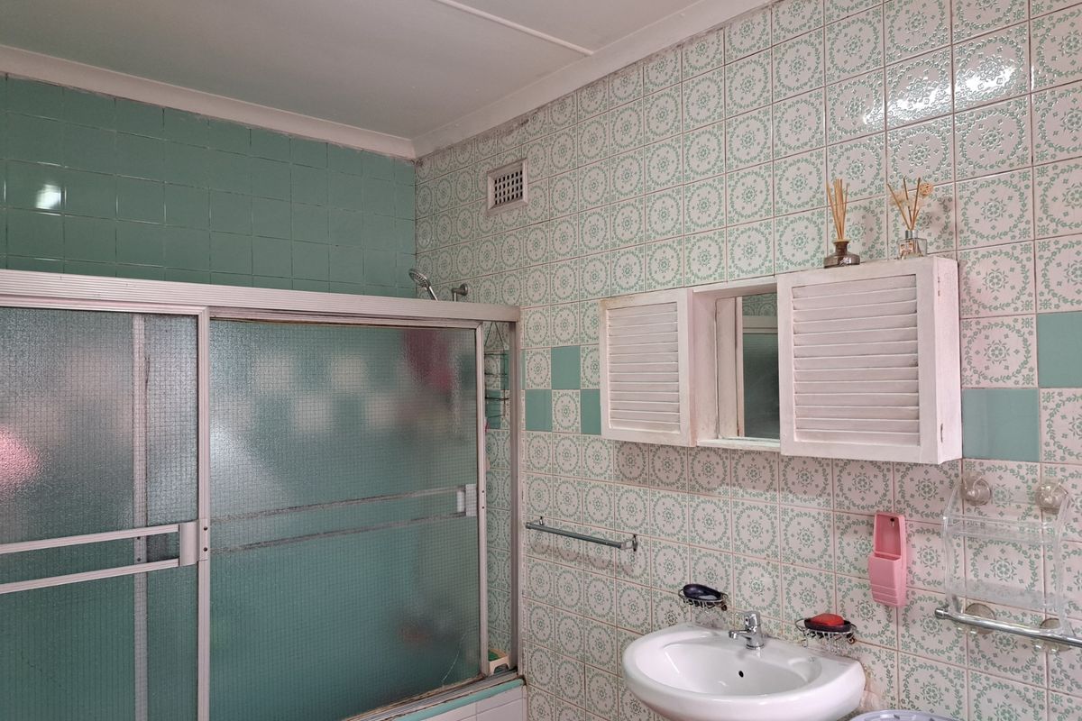A dated bathroom featuring a pedestal basin, shower enclosure with sliding doors, and patterned wall tiling throughout.