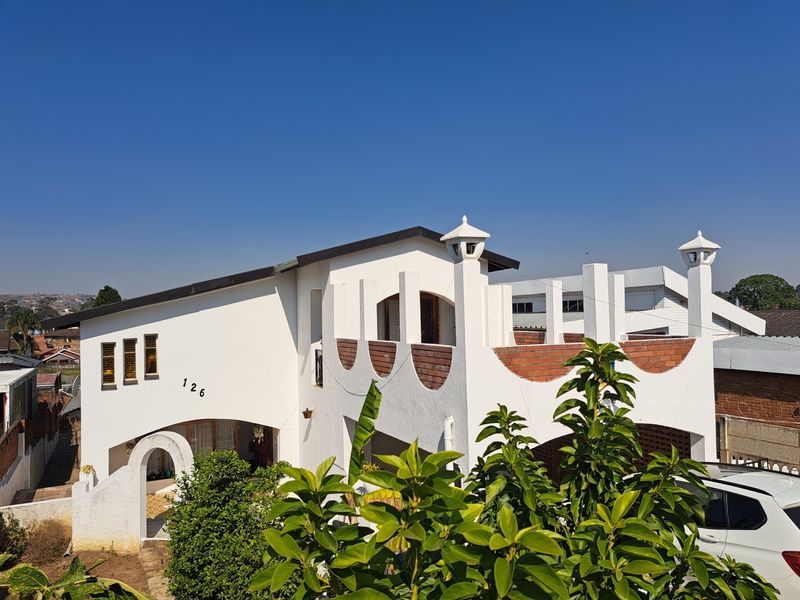 A unique two-story house featuring a distinctive arched entrance, decorative brickwork on the balcony, and a clean white stucco exterior finish.