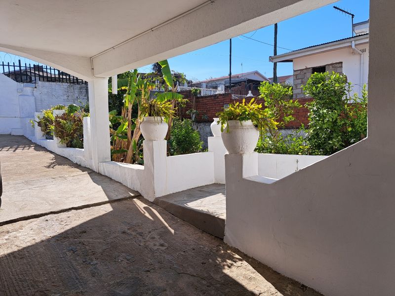 A covered outdoor patio area featuring concrete flooring and masonry boundary walls, providing a functional space for outdoor relaxation.