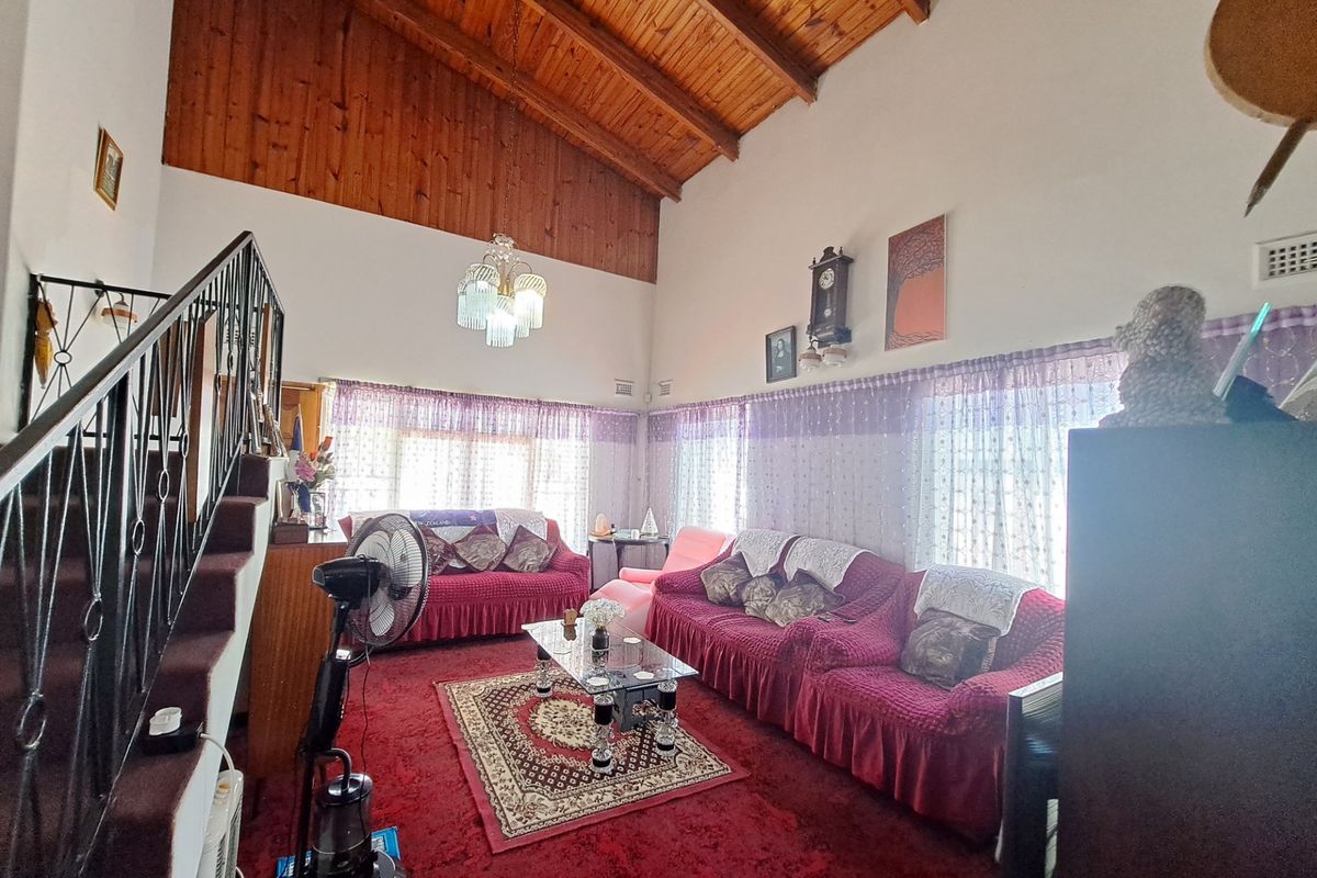 Spacious living room featuring a high exposed timber raked ceiling and a wrought iron staircase, offering a unique architectural character ready for modern updates.