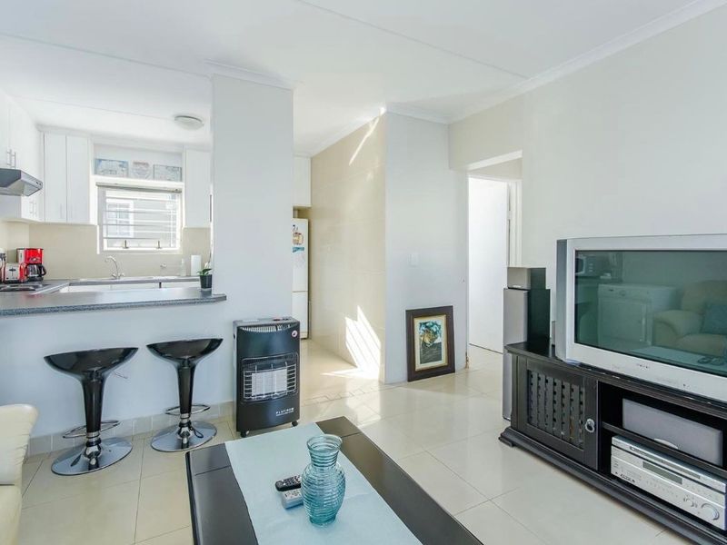 Open-plan living area featuring a functional kitchen with breakfast bar, tiled flooring, and neutral finishes, creating a bright and connected living space.