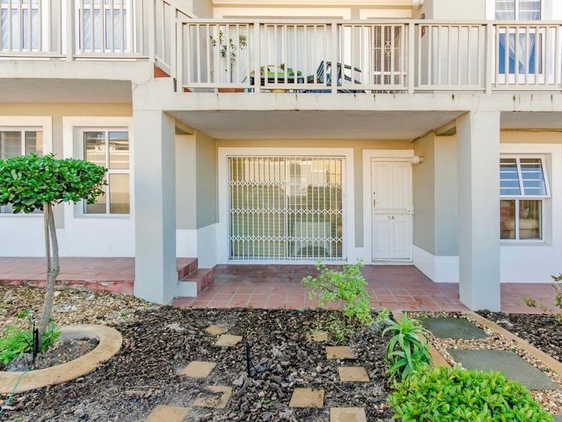 Ground floor patio area with tiled flooring, security gate access, and an overhead balcony, set within a landscaped garden environment.