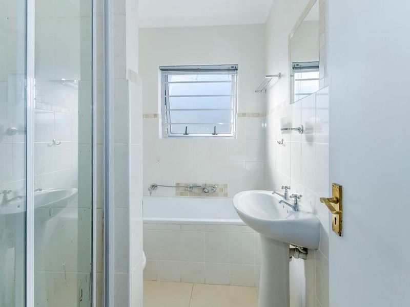 A functional bathroom featuring a pedestal basin, bathtub, and separate shower enclosure with neutral wall tiling and a louvered window for ventilation.
