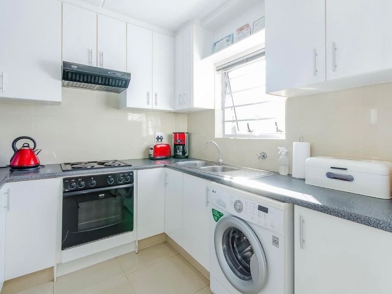 A functional kitchen featuring white cabinetry, dark laminate countertops, a built-in oven with hob, extractor fan, and integrated laundry plumbing.