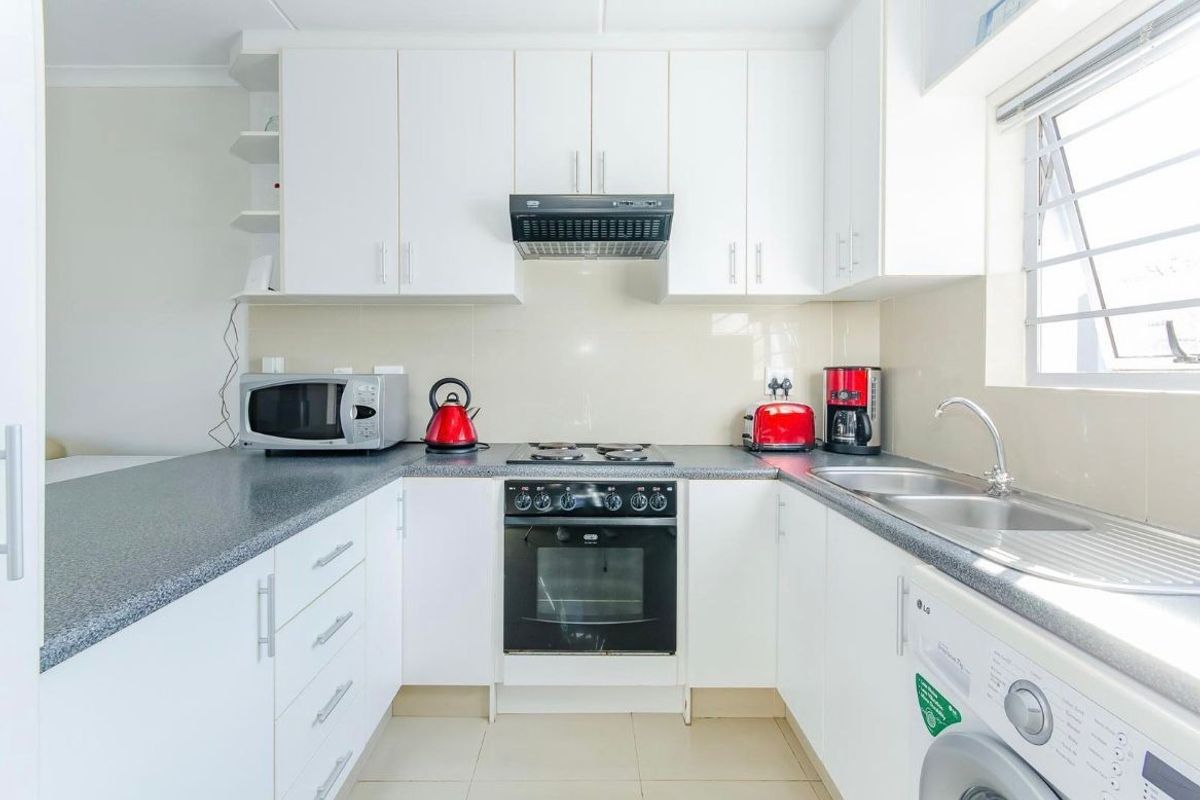 A clean and functional kitchen featuring white cabinetry, a dark laminate countertop, built-in oven with hob, and a double sink with tiled splashback.