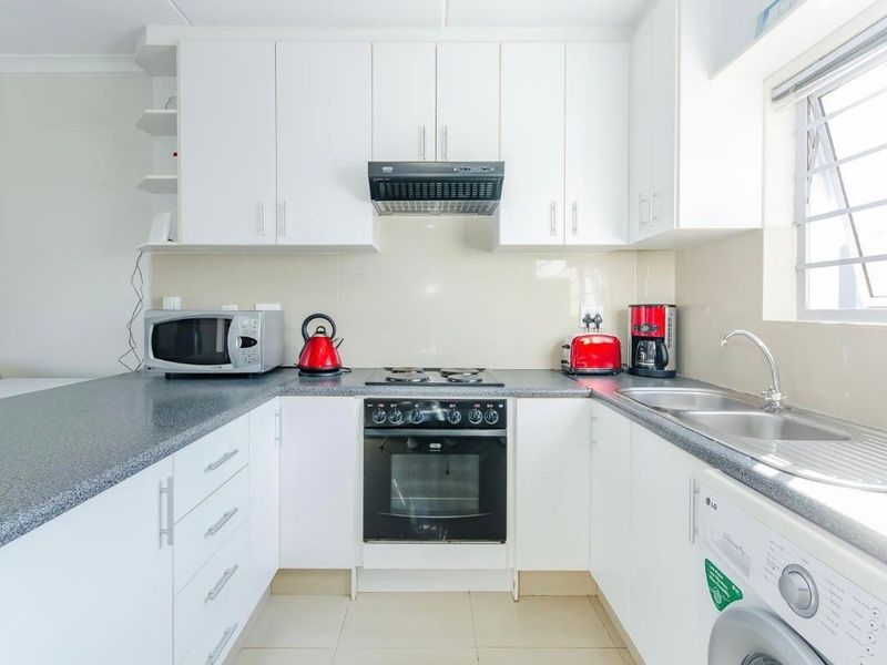 A clean and functional kitchen featuring white cabinetry, a dark laminate countertop, built-in oven with hob, and a double sink with tiled splashback.