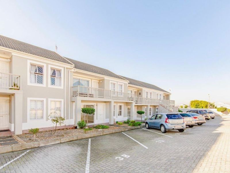 Front elevation of a multi-story apartment complex featuring paved parking bays, balconies, and well-maintained exterior finishes.