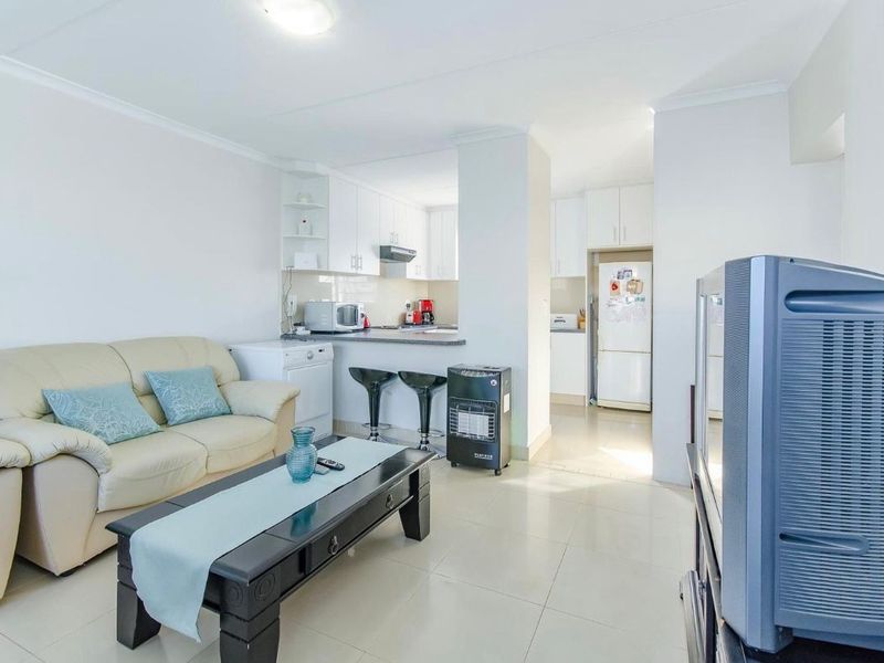 An open-plan living and kitchen area featuring tiled flooring, white cabinetry, and a breakfast bar, creating a functional and connected living space.