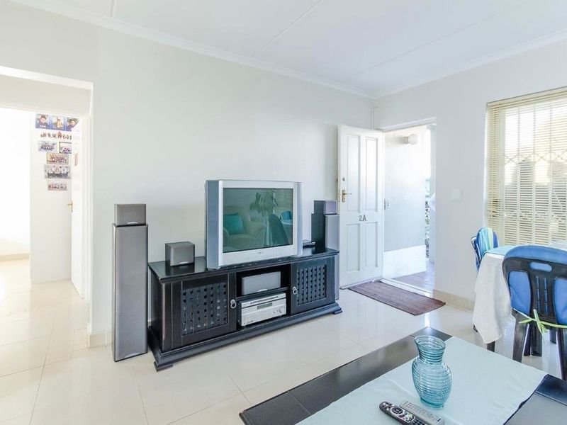 A bright living room featuring neutral tiled flooring, white walls, and natural light through a window with venetian blinds.