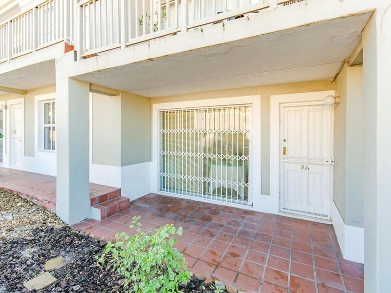 Ground floor patio area featuring tiled flooring, security gate access, and overhead balcony structure.