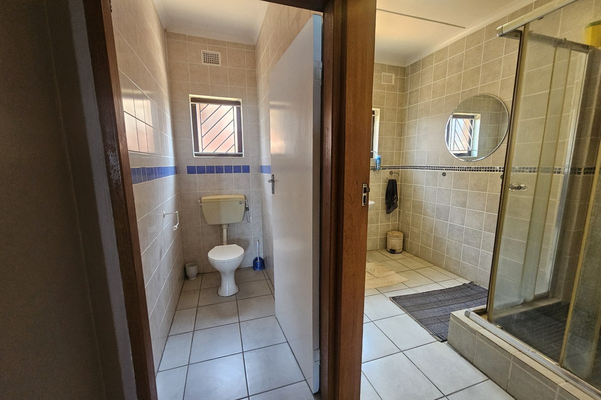 A functional bathroom featuring a separate toilet area and a shower enclosure with neutral wall and floor tiling.