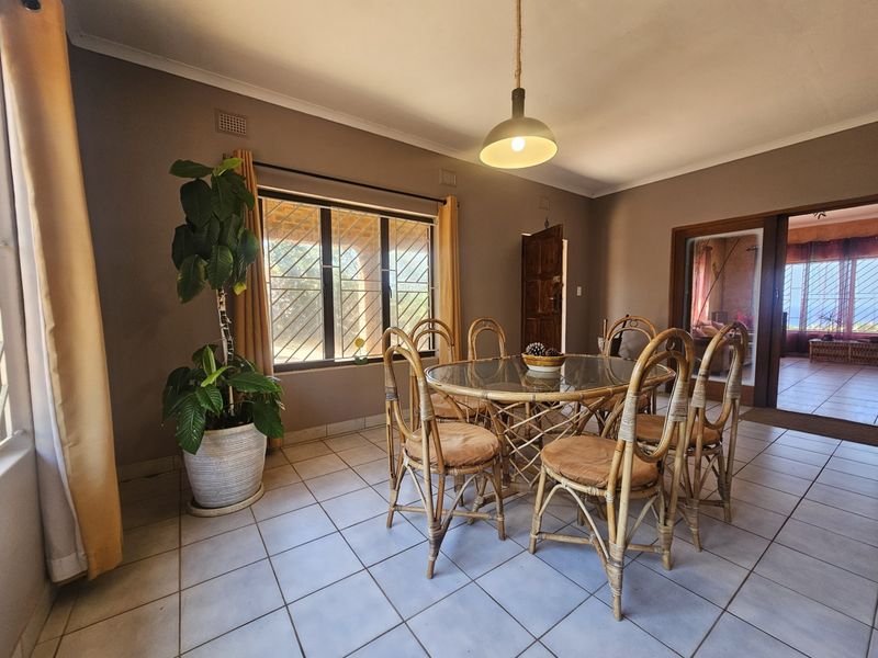 A dining room featuring tiled flooring, a pendant light fixture, and security bars on the windows, with an open transition to an adjacent living space.