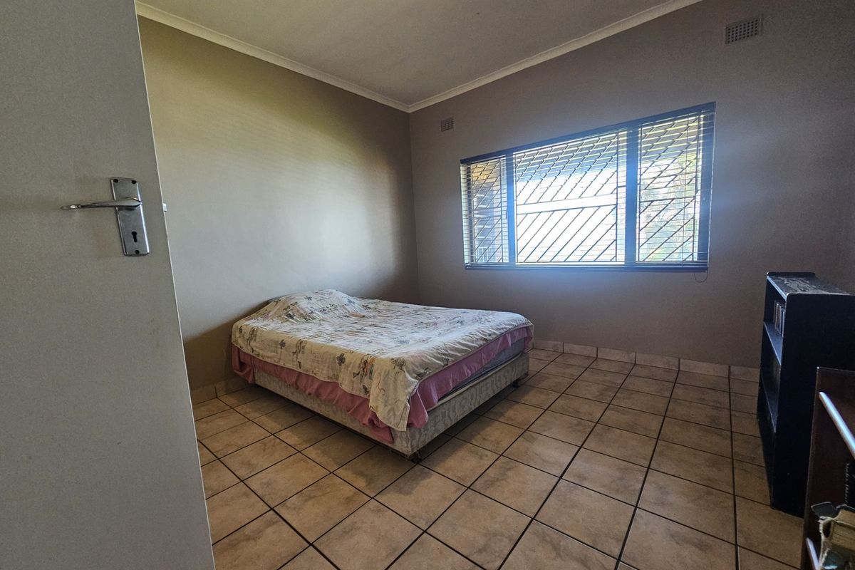 A bedroom featuring tiled flooring, security bars on the window, and cove cornicing, offering a functional space with potential for cosmetic updates.