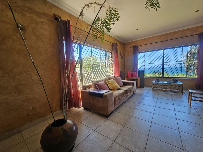 Spacious living room featuring tiled flooring, textured walls, and large windows with security bars offering scenic ocean views.