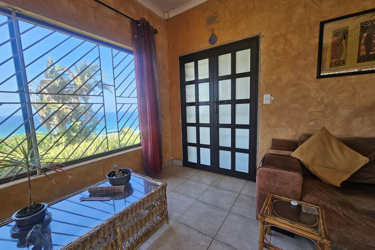 A living room featuring tiled flooring, textured walls, and large windows with security bars, offering a view of the ocean.