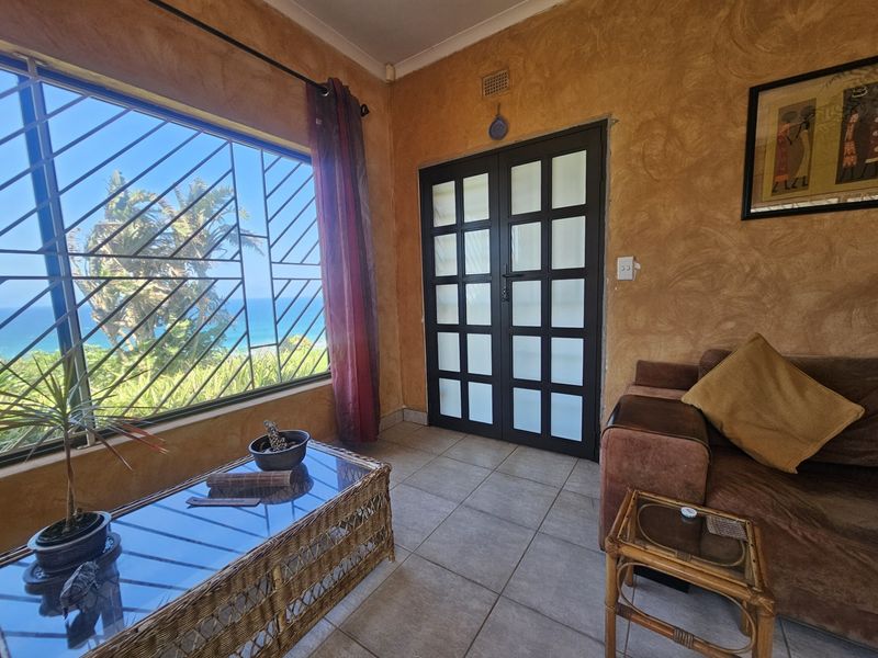 A living room featuring tiled flooring, textured walls, and large windows with security bars, offering a view of the ocean.