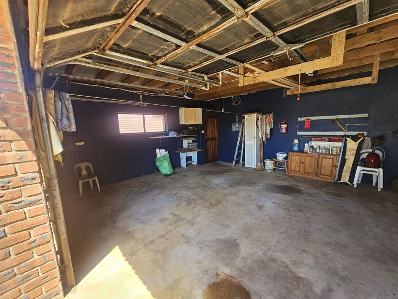 A spacious double garage featuring exposed timber roof beams, concrete flooring, and direct access to the home, offering potential for storage or workshop use.