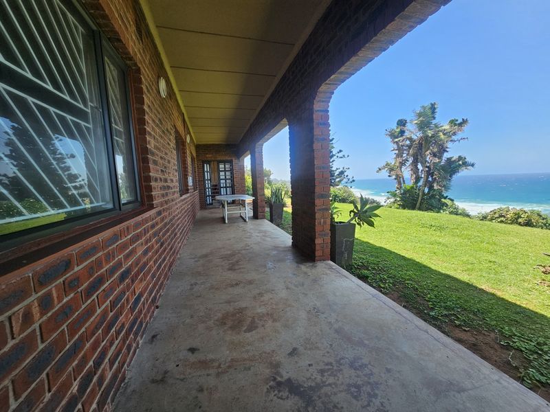A covered brick veranda featuring arched pillars and concrete flooring, offering expansive ocean views and direct access to the garden.