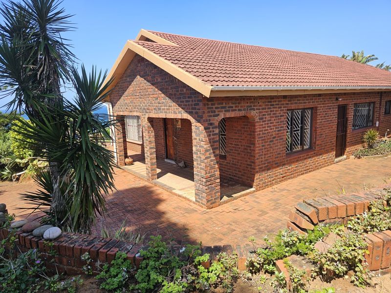 A rear view of a face brick house featuring a covered patio, tiled roof, and paved courtyard area.