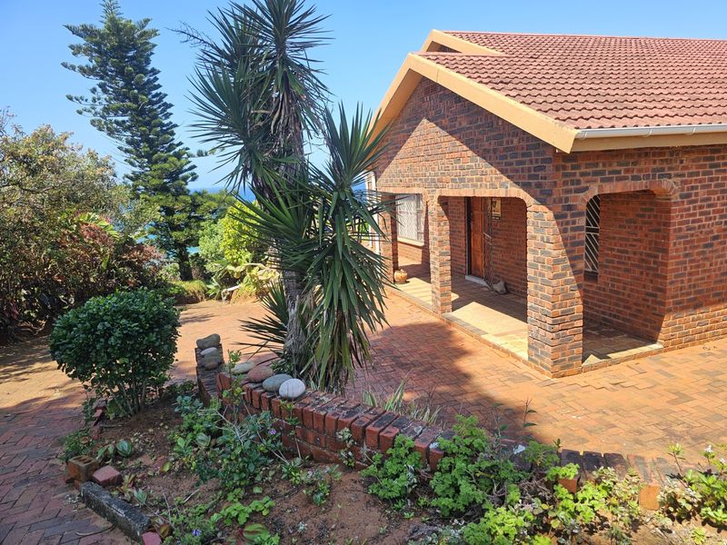 A rear view of a face brick house featuring a covered patio, paved outdoor area, and established garden.