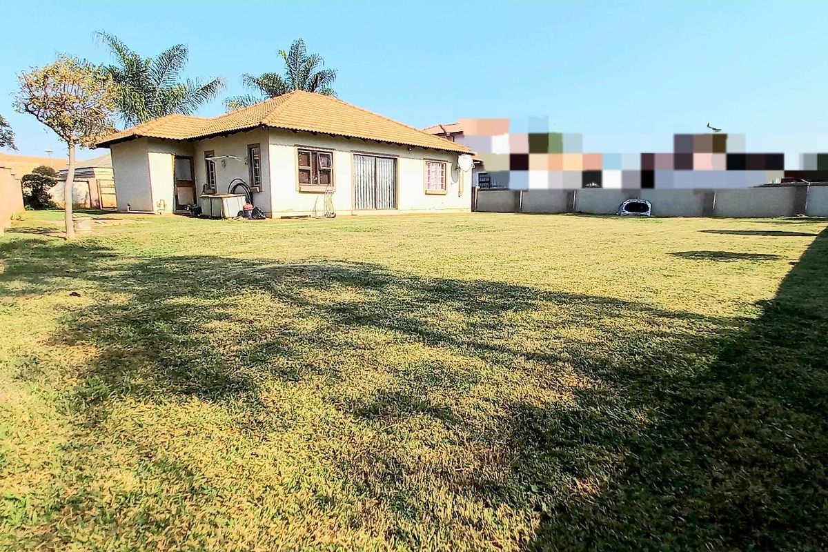 A spacious rear garden area featuring a large lawn, perimeter boundary walls, and a view of the rear elevation of the house.