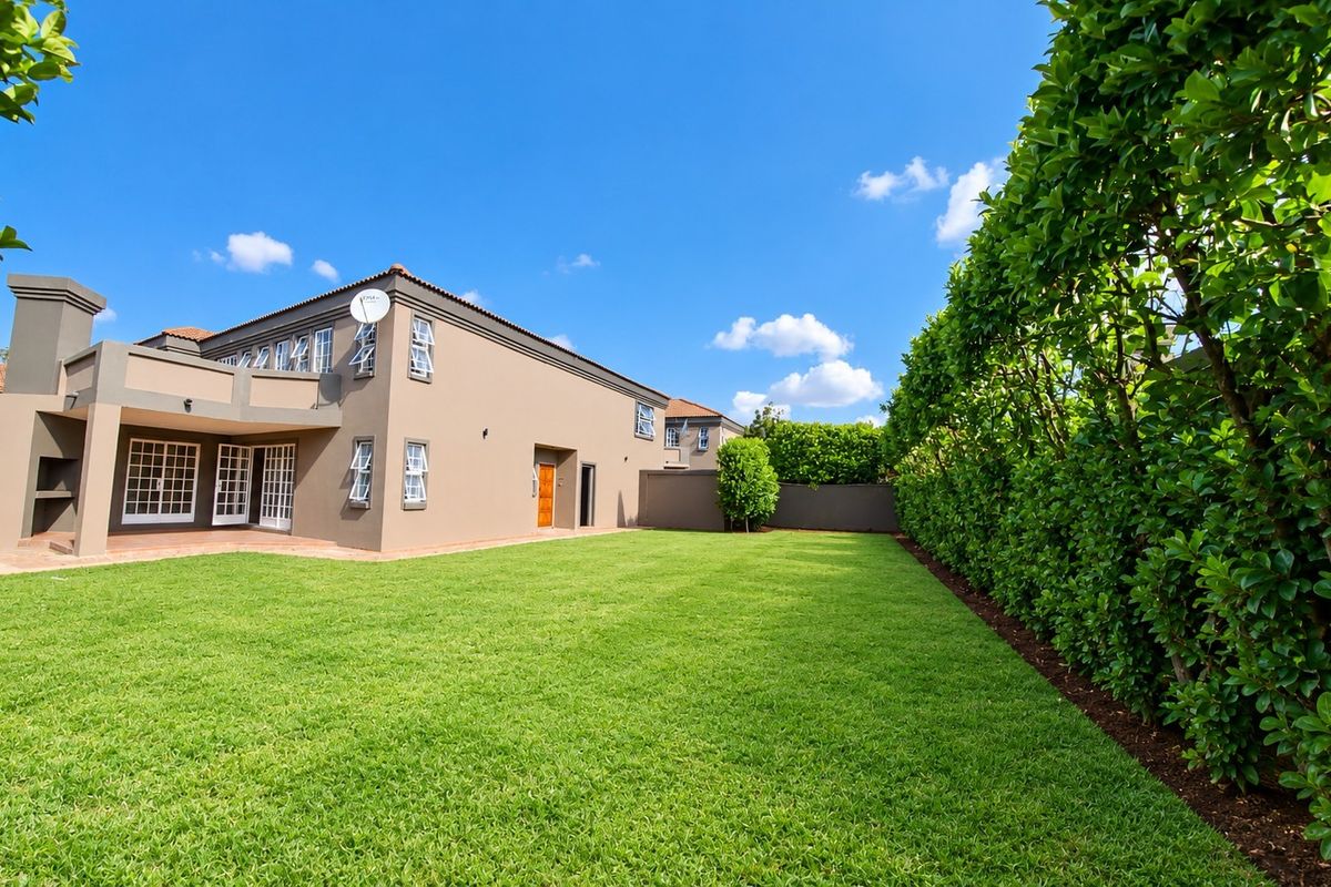 Spacious rear garden featuring a well-maintained lawn, tall privacy hedges, and a covered patio area with a built-in braai.