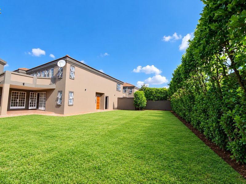 Spacious rear garden featuring a well-maintained lawn, tall privacy hedges, and a covered patio area with a built-in braai.