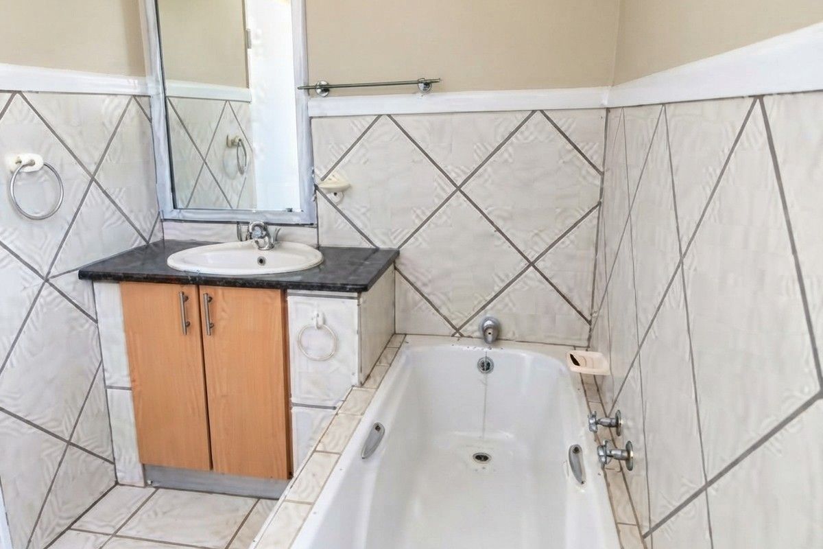 A functional bathroom featuring a built-in vanity with integrated sink, a standard bathtub, and diamond-patterned wall tiling.