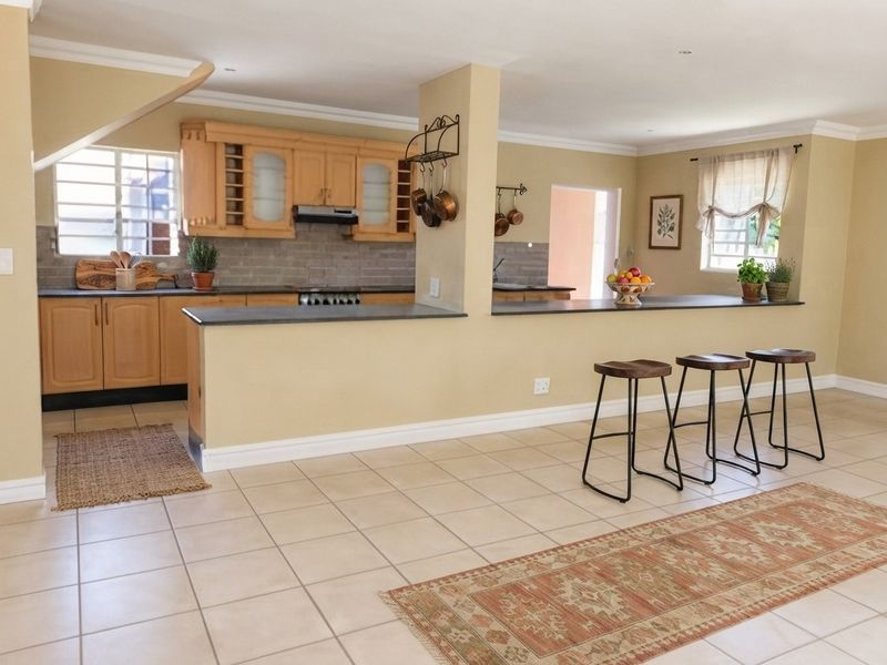 Open plan kitchen featuring light wood cabinetry, stone countertops, and a breakfast bar, seamlessly integrated with the living area on tiled flooring.