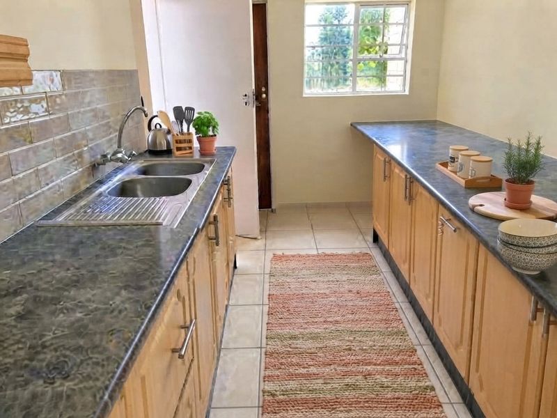 A functional galley-style kitchen featuring wooden cabinetry, laminate countertops, a double basin sink, and tiled flooring with a window for natural light.