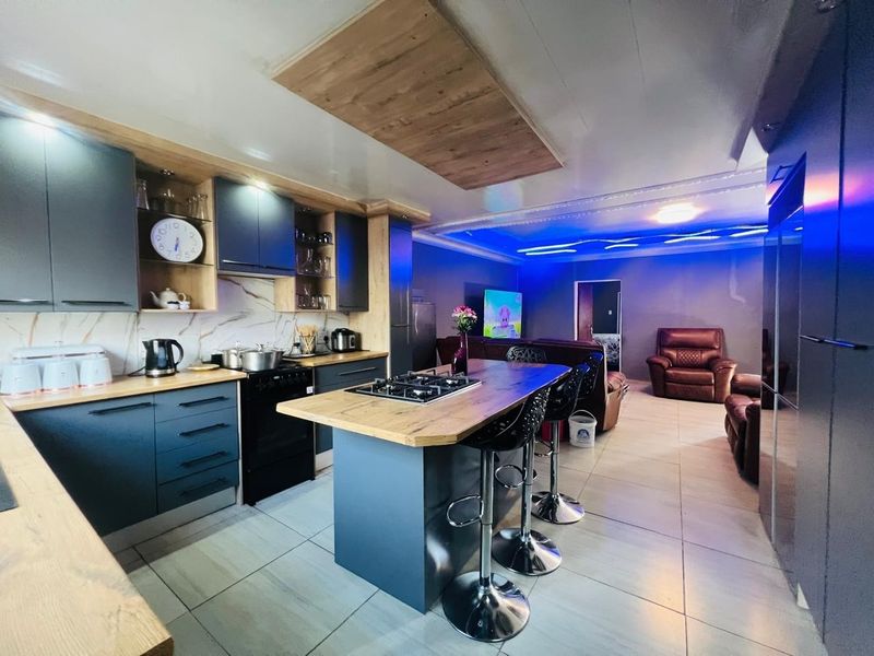 Modern open-plan kitchen and living area featuring dark cabinetry, a central island with a gas hob, and contemporary recessed ceiling lighting.