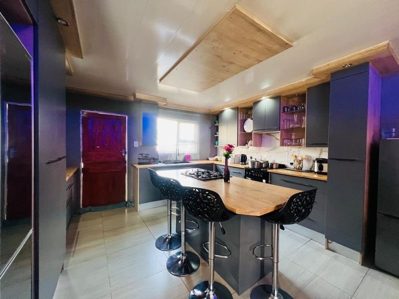Modern kitchen featuring dark cabinetry, a central island with a gas hob, stone countertops, and tiled flooring with unique ceiling detailing.